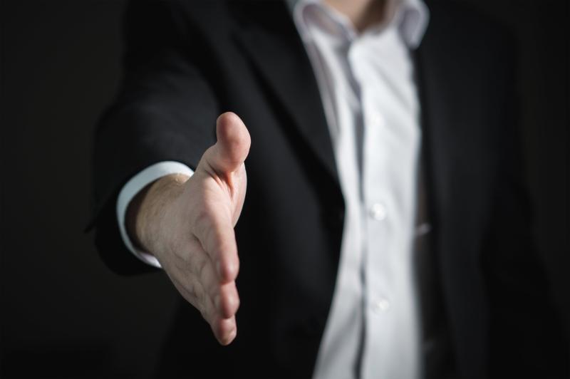 A picture that shows on the foreground the hand of a lobbyist wearing a suit and a white shirt, ready to shake another hand.