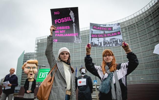 Two young activists holding signs saying ¨No fossil lobbies in my Parliament" and "Plastic is Big Oil's plan B" in a rally in front of the EU Commission. 